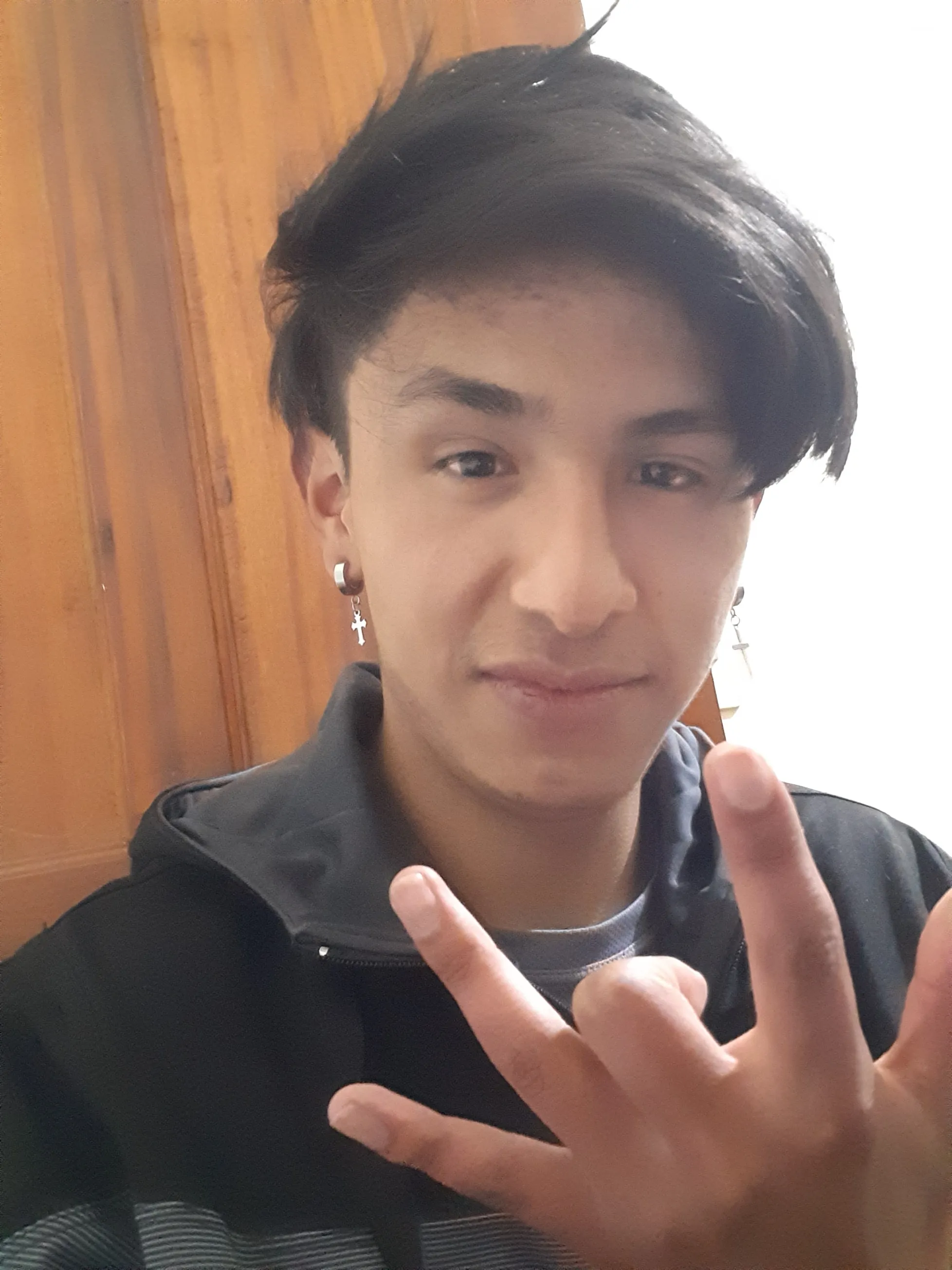 A professional portrait of a young Hispanic male software developer with a friendly and confident expression. He is wearing a modern casual hoodie, set against a blurred, warmly lit indoor background. The lighting is soft and flattering, highlighting his features with a professional studio quality that conveys reliability and technical expertise.
